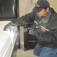 Bed bug inspection technician checking a mattress and bed frame for signs of infestation in West Palm Beach, FL