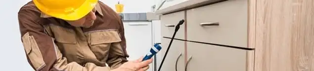 Roach exterminator applying treatment under kitchen cabinets in West Palm Beach, FL