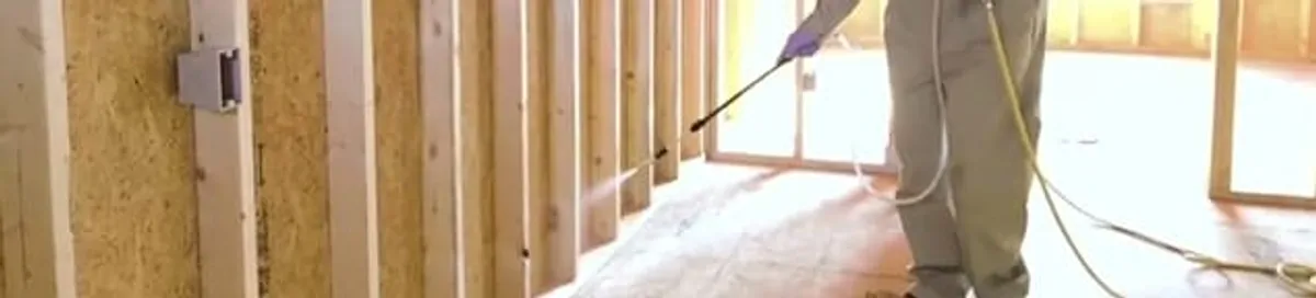 Termite treatment technician applying spray along framing and unfinished walls in West Palm Beach, FL