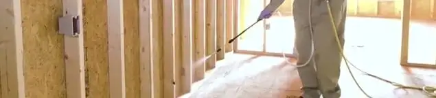 Termite treatment technician applying spray along framing and unfinished walls in West Palm Beach, FL